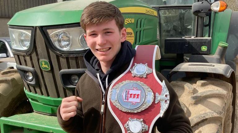 Edward posing with one of his belts in front of a tractor