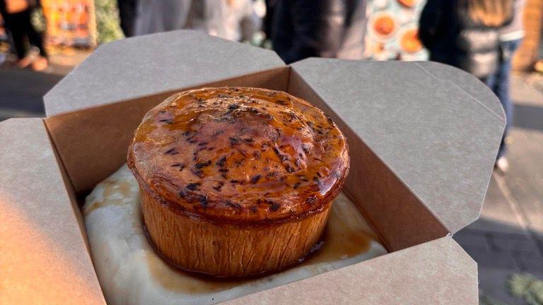 Pie and mash, covered with gravy, in a cardboard takeaway box.