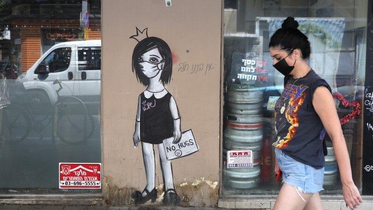 A woman walks by coronavirus graffiti in Tel Aviv (8 September 2020)