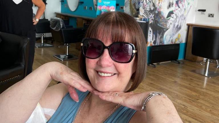 Close-up of Sharon Price at a salon, wearing sunglasses and smiling at the camera