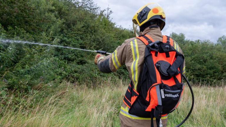 A firefighter with a backpack spraying a jet of water into a field