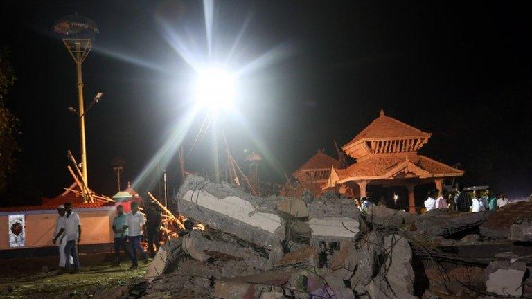 People walk past the damaged buildings at the spot where a massive fire broke out during a fireworks display at the Puttingal temple complex in Paravoor village, Kollam district, southern Kerala state, India, Sunday, April 10, 2016.