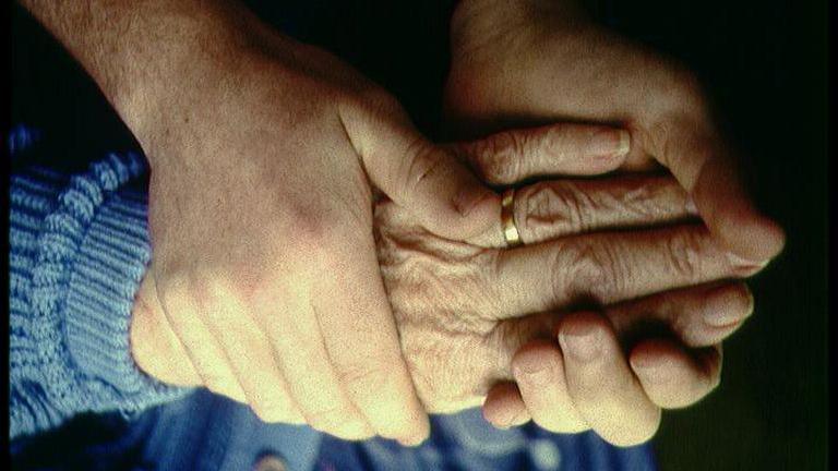 A close up of an elderly persons hand being held by two younger hands. 