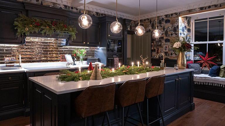 A kitchen decorated with Christmas decorations. Candles line the kitchen island with foliage.