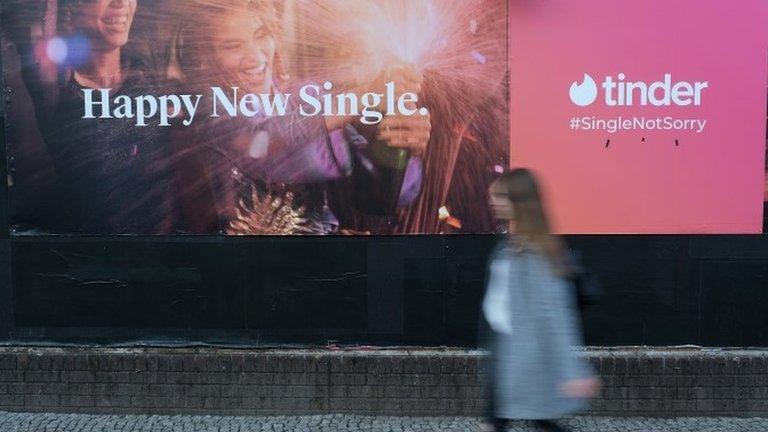 A young woman walks past a billboard advertisement for the dating app Tinder