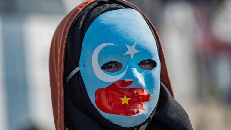 A protester against China's actions in Xinjiang wears a mask with the colours of the flag of East Turkestan