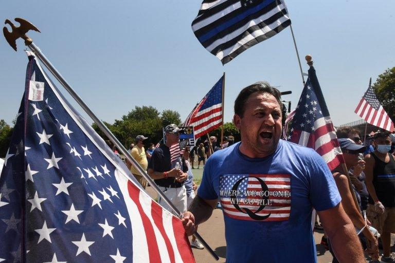 A person wearing a t-shirt supportive of QAnon at a rally with US flags