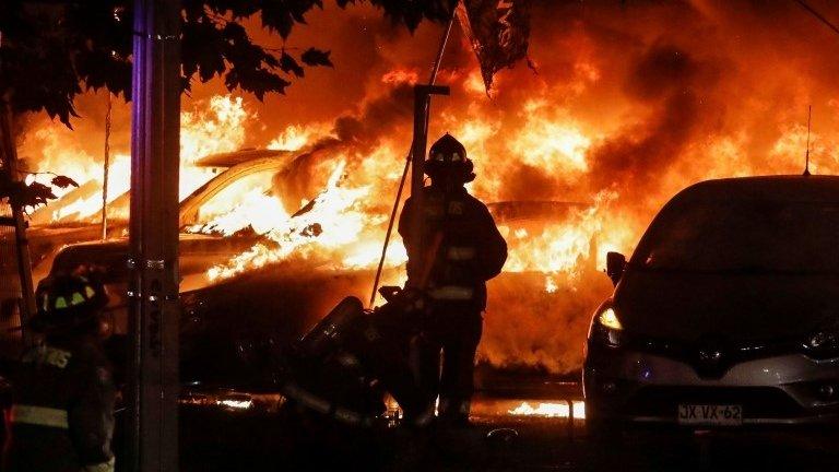 A firefighter is seen next to the cars on fire during a protest against Chile"s government in Vina del Mar, Chile February 23, 2020