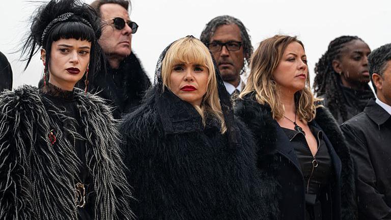 Celebrities dressed in black attending a "funeral" in an episode of The Celebrity Traitors. Paloma Faith and Charlotte Church are in the front row, with Jonathan Ross and David Olusoga behind.