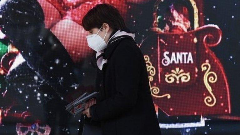 A woman wearing a face mask walks by the window of a shop in Milan