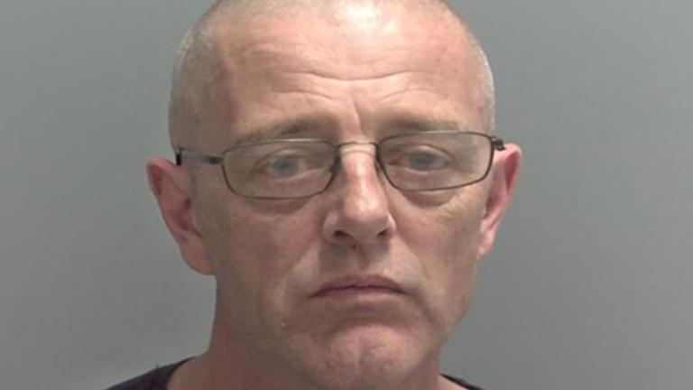 A police mugshot of Timothy Neale looking straight at the camera, he is wearing a dark top and wearing glasses