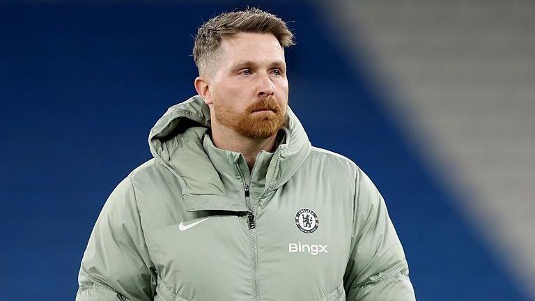 Calum McFarlane wearing a grey coat with a Chelsea badge on the chest