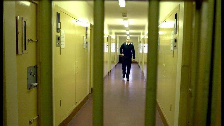 Prison wing with barred gate in the foreground and prison officer