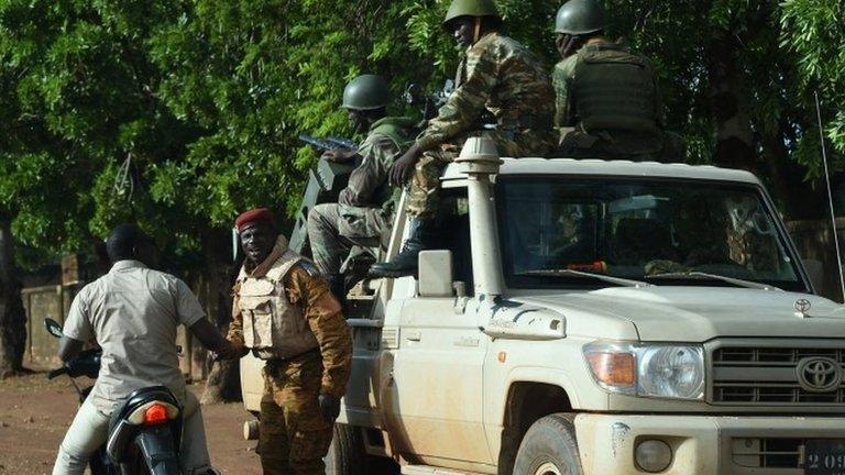 A man riding a motorcycle speaks with a member of Burkina Faso army troops standing guard outside Sangoule Lamizana military camp in Ouagadougou on 22 September 2015