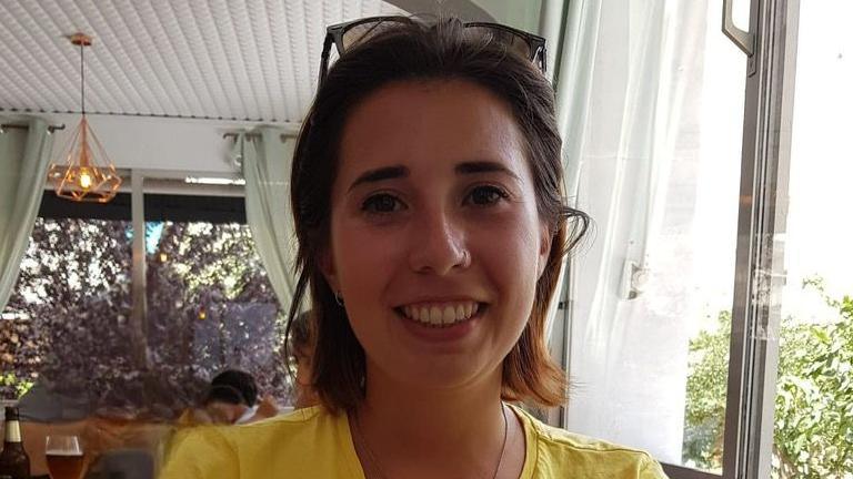 Marta Elena Vento is seated in a dining room. She has short, dark hair and wears a yellow top and sunglasses on top of her head.