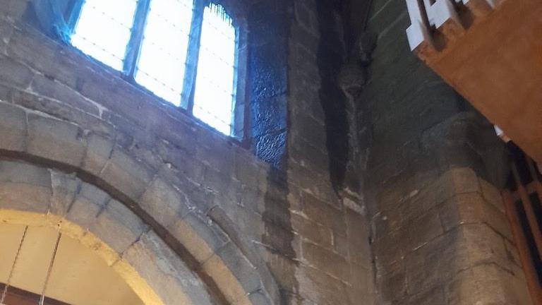 Water running down the inside of a church from its roof near a stained glass window