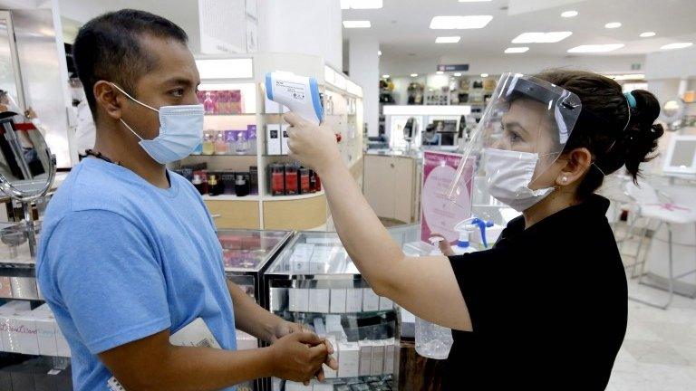 A woman takes the temperature to a customer at the entrance of a store in Guadalajara, Jalisco State, on June 1, 2020 after Mexico began gradually reopening its economy after more than two months of shutdown because of the COVID-19 coronavirus pandemic.