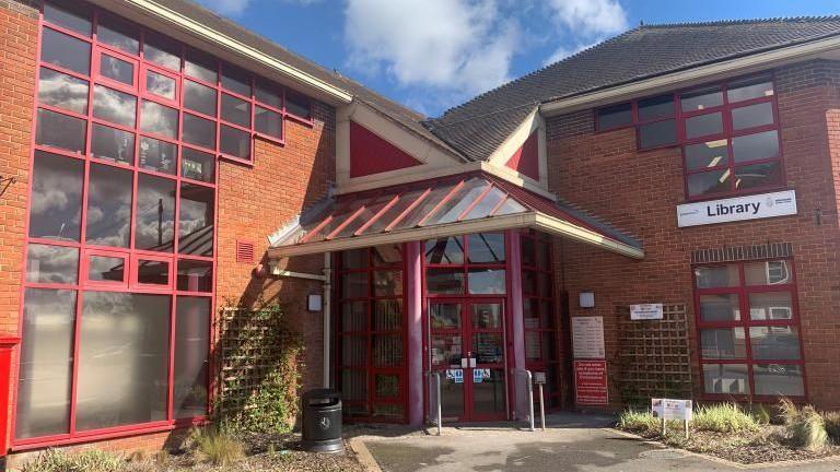 An L-shaped, two storey brick building with red windows and doors.