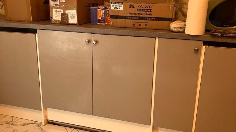 Grey kitchen cabinets, with closed doors, hiding a lift, with boxes and items on the top.