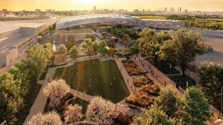 An artist's impression of the exterior of the new HS2 Old Oak Common station. The interlocking curved roofs over the platforms can be seen, with the London skyline lit by bright sunshine in the background. There are lawns surrounded by trees and criss-crossed by paths in the approach to the station.