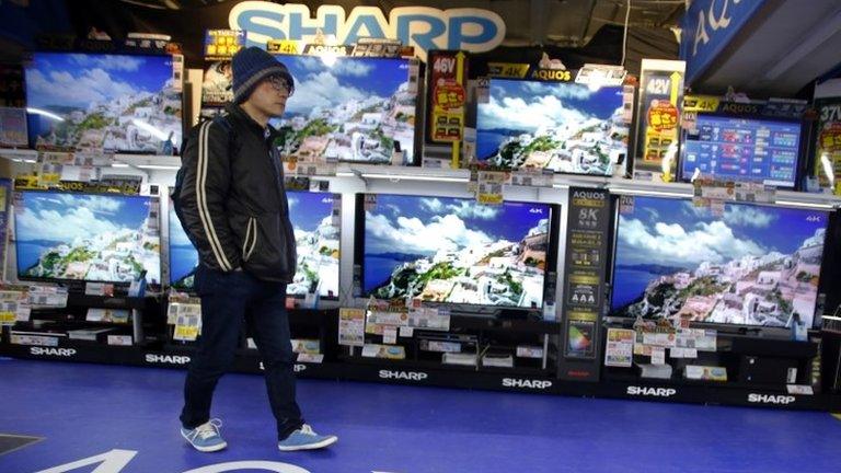 A shopper walks in front of Sharp"s Aquos flat-panel TVs at an electronics store in Tokyo, Thursday, Feb. 25, 2016