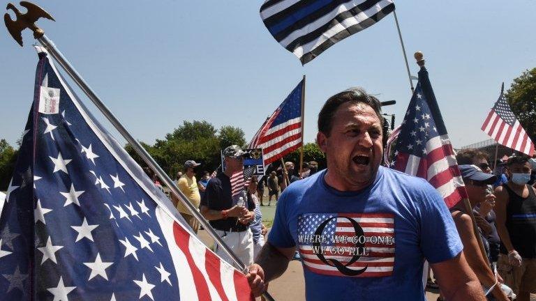 A person wearing a t-shirt supportive of QAnon at a rally with US flags