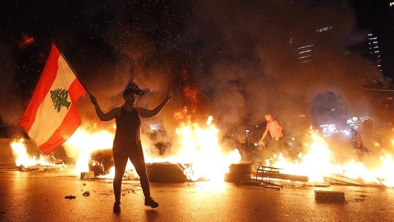 An anti-government protester carries a Lebanese flag as other protesters burn tires and block the main motorway during a protest against the economic conditions in the Jal El Dib area north of Beirut, Lebanon, on 11 June 2020