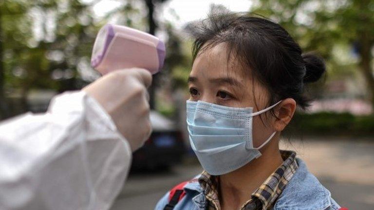 A man wearing a protective suit checks a woman's temperature next to a residential area in Wuhan, in China"s central Hubei province on April 7, 2020.