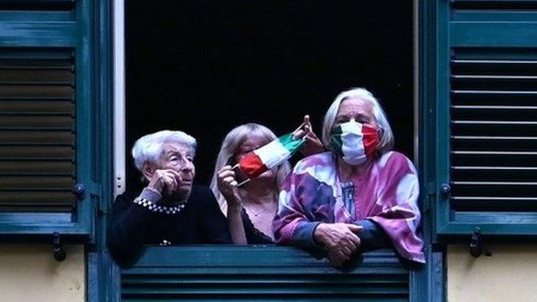 People with protective masks look from their windows at artists performing in the courtyard of a popular apartment building in Rome