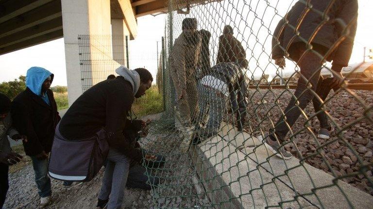 Migrants climb through a fence on to the tracks near the Eurotunnel site at Coquelles in Calais, France.