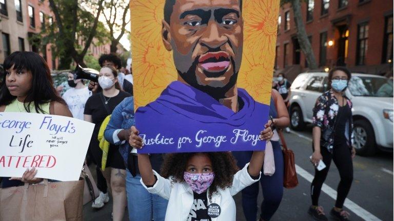 A little girl holds a placard with the words "Justice for George Floyd"