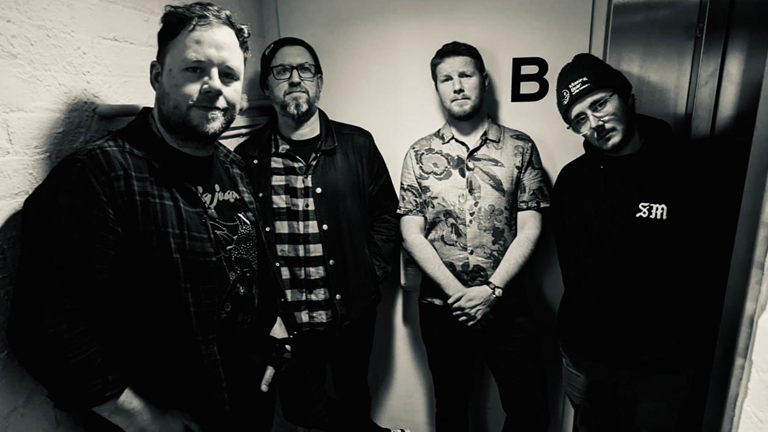 A black and white picture of the four members of Sinews in a corridor, posing for a band photo.