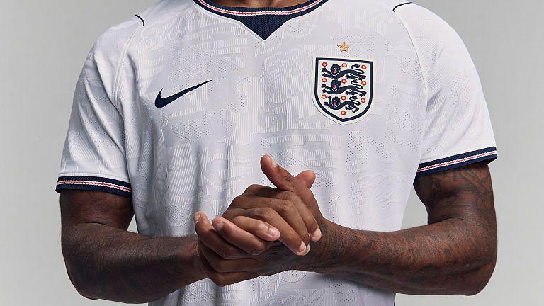 Marcus Rashford clasps his hands while modelling England's white Nike home shirt for the 2026 Fifa World Cup