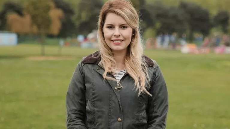 Kim McGuinness, pictured from the waist up, wearing a dark green Barbour coat. She has long blonde hair and is looking into the camera smiling.