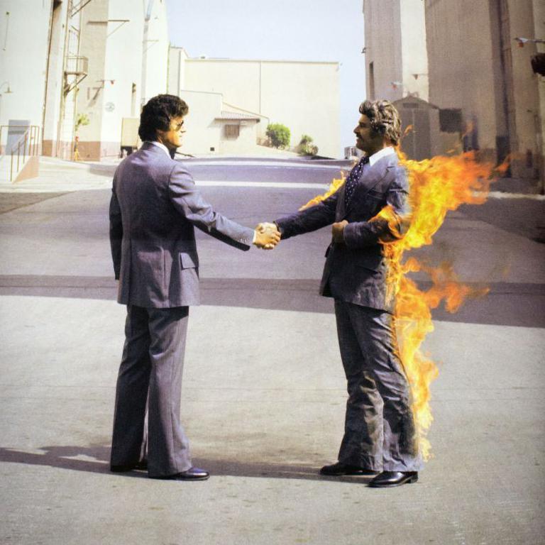 Two men wearing suits shake hands - one of them is on fire