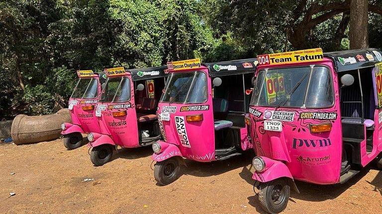 Four rickshaws painted pink are parked side by side on a beach in India.