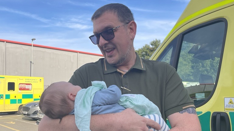 A paramedic with sunglasses on holds a baby smiling.