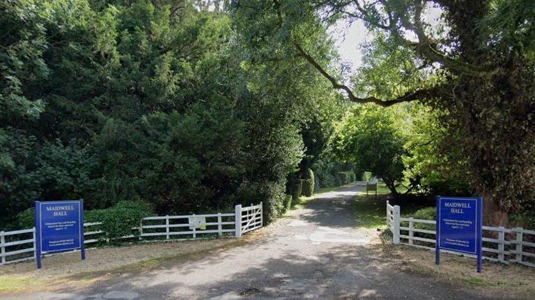 Entrance to school showing blue signs and driveway lined with trees