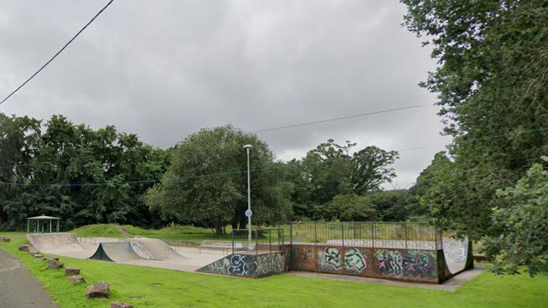 Skatepark in Okehampton. Graffiti is on the side of the skatepark. Grass is surrounding the site.
