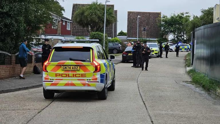Four police cars and seven police officers standing in a quiet road.