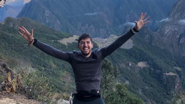 a man with arms outstretched and a big smile, with mountains in the background