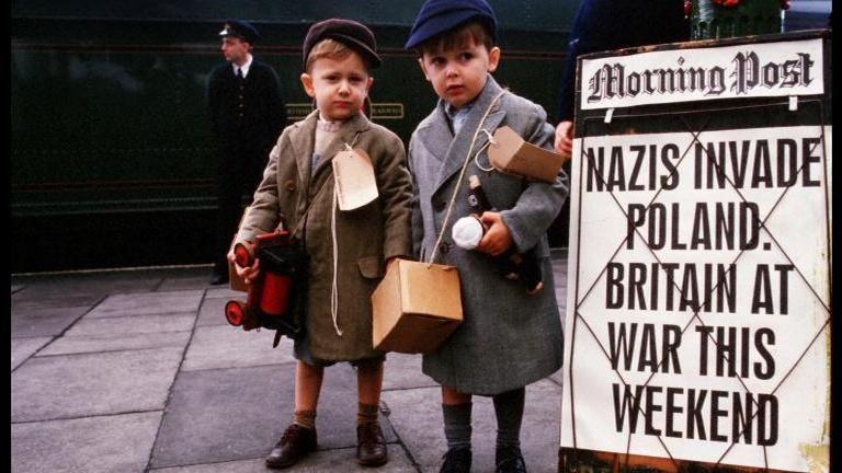 Two boys next to newspaper billboard which says "Nazis invade Poland."