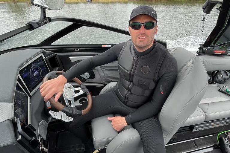 Man in a wetsuit sitting at the wheel of a small boat
