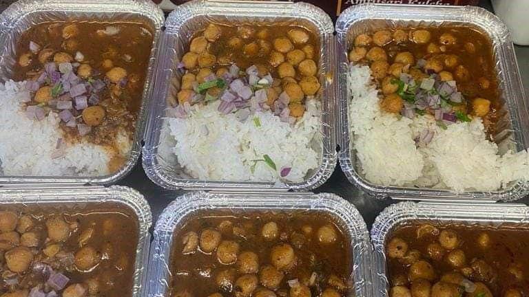 Six portions of curried brown chickpeas and white rice in silver boxes.