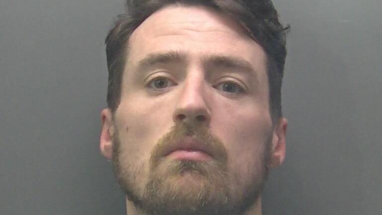 A custody photo of Mark Moss, who is positioned against a plain, grey background. He has short, dark hair that appears neatly styled, with the top slightly voluminous and the sides trimmed closer. His ears are visible on both sides.