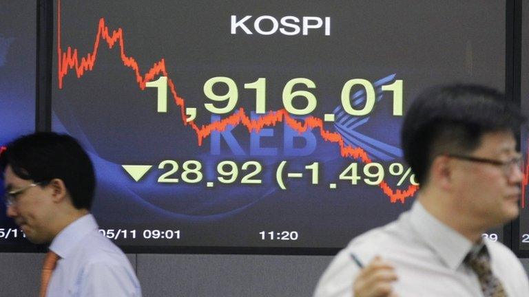 Currency dealers walk past a stock-price board in Seoul, South Korea, on 11 May 2012