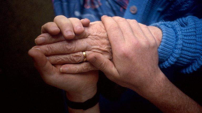 Elderly woman's hand being held by a carer