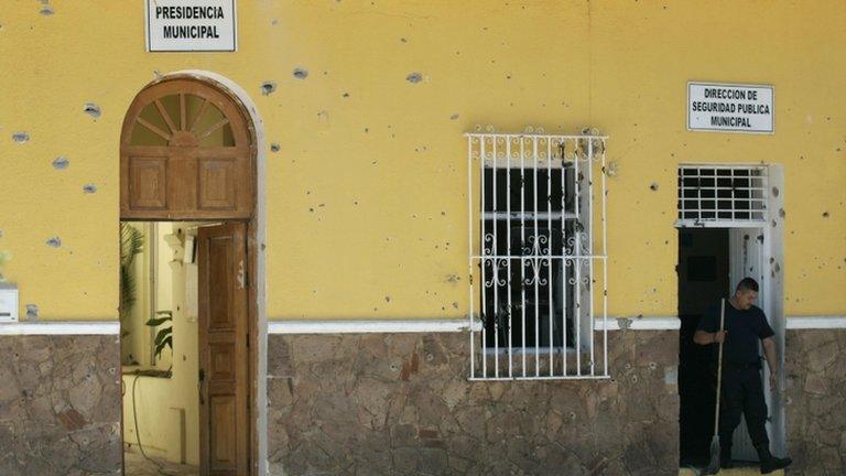 A policeman holds a broom as he leaves the bullet-riddled police station located in the town hall of San Cristobal de las Barrancas