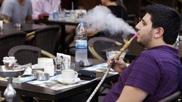 A man outside a coffee shop in Beirut smokes a water pipe