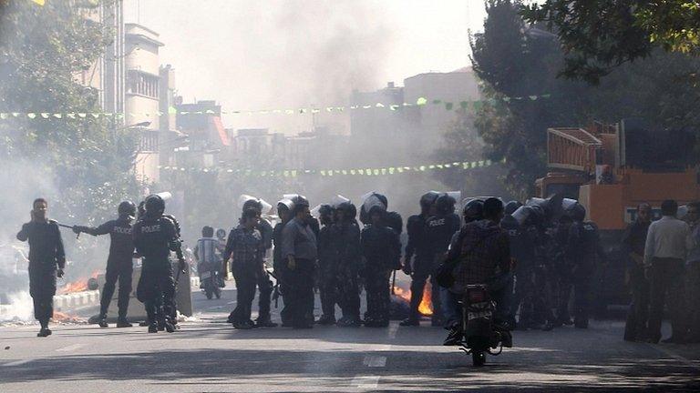 Iranian riot police stand next to a rubbish bin set on fire by protesters in central Tehran, near the main bazaar (3 Oct)